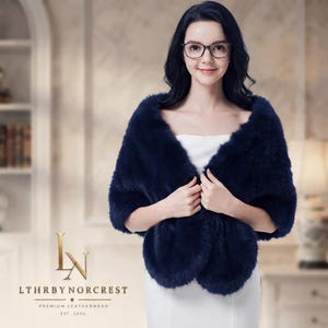 May include: A navy blue faux fur stole worn over a white strapless garment. The stole features a thick, plush texture and wraps around the shoulders. The logo for LTHRBYNORCREST PREMIUM LEATHERWEAR EST. 2024 is visible in the bottom left corner.