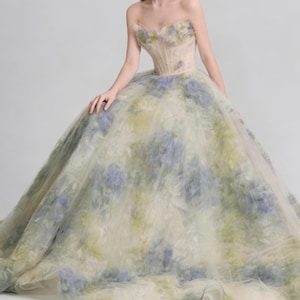 May include: A strapless, floral-patterned gown with a fitted bodice and a full, flowing skirt. The dress features a soft color palette of cream, blue, and green, creating a dreamy, ethereal look. The gown is suitable for a wedding or formal event.