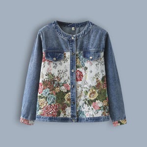 Peut inclure: Veste en jean bleu clair avec un panneau avant et des poignets en tapisserie florale. La veste a un col rond, deux poches de poitrine et des fermetures à boutons. Le motif floral présente des roses et d'autres fleurs.