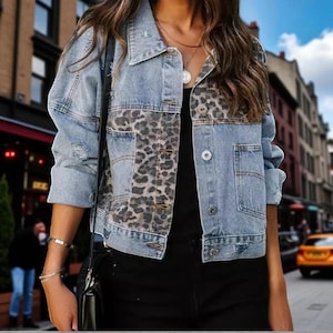 May include: Pale blue denim jacket with leopard print sections. The jacket has a traditional collar, button fastenings, and front pockets. Distressed elements give a vintage feel. A fashionable outerwear item.