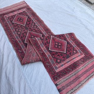 Könnte beinhalten: Ein rechteckiger, handgewebter Teppich mit einem geometrischen Muster in Rot-, Schwarz- und Grautönen. Der Teppich hat Diamanten- und Rechteckformen mit einem Fransenrand. Der Teppich ist etwa 152 cm lang.