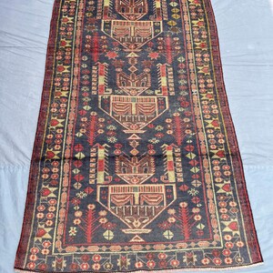 Può includere: Un tappeto rettangolare, tessuto a mano, con un campo centrale blu scuro e intricati motivi geometrici in rosso, beige e giallo. Il tappeto presenta un design a medaglione centrale e un bordo con motivi floreali.