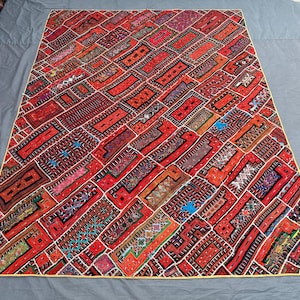 Op de afbeelding: Een levendig, rechthoekig patchwork tapijt met een complex ontwerp. Het tapijt heeft een verscheidenheid aan rode, oranje en bruine rechthoekige patches, elk met unieke patronen en kleuren. De randen zijn omlijnd in een crème kleur, wat een opvallend contrast creëert.