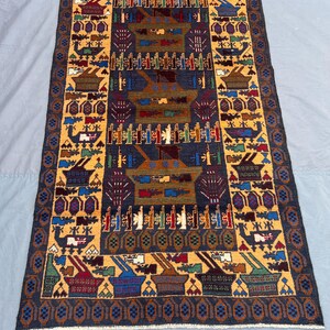 May include: A rectangular, hand-woven rug with a central design in navy blue, gold, and brown. The rug features repeating geometric patterns and stylized motifs, including vessels and floral elements. The border is a dark blue with a repeating pattern.