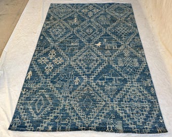 Könnte beinhalten: Ein rechteckiger Teppich mit tiefblauem Hintergrund und einem sich wiederholenden weißen geometrischen Rautenmuster. Das Design enthält komplexe Linienzeichnungen von Kamelen, Vögeln und menschlichen Figuren innerhalb der Rauten.