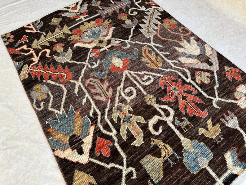 K&ouml;nnte beinhalten: Ein rechteckiger Teppich mit dunkelbraunem Hintergrund und einem sich wiederholenden Muster aus stilisierten Blumenmotiven und Vogelfiguren in Rot-, Blau-, Beige- und Graut&ouml;nen, angeordnet in einem symmetrischen, rankenartigen Design.