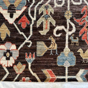 K&ouml;nnte beinhalten: Ein dunkelbrauner Teppich mit einem gewebten Muster aus stilisierten Blumen, V&ouml;geln und geometrischen Formen in Rot-, Blau-, Beige- und Wei&szlig;t&ouml;nen. Das Design enth&auml;lt komplexe, verzweigte Linien, die die verschiedenen Blumen- und Tiermotive verbinden.