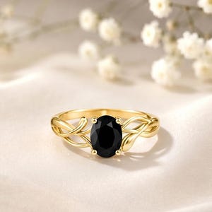 May include: A gold ring featuring an oval-cut black gemstone set in the center. The band is crafted with a delicate, intertwining vine-like design that branches out from the central setting, creating a continuous, flowing metal structure.