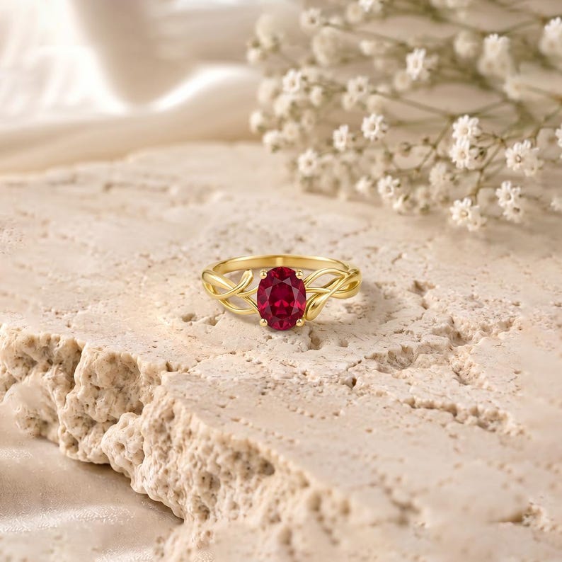 K&ouml;nnte beinhalten: Ein Goldring mit einem zentralen, oval geschliffenen, tiefroten Edelstein, der von vier Krappen gehalten wird. Die Ringschiene ist mit einem filigranen, rankenartigen Design gestaltet, das vom Ringkopf ausgeht und eine organische Optik erzeugt.