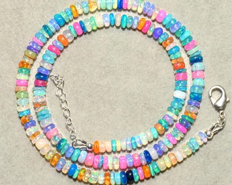 May include: A colorful necklace composed of small, round opal beads in a variety of colors, including pink, blue, orange, and green. The necklace has a silver clasp and chain. The beads are strung together to form a circular shape.