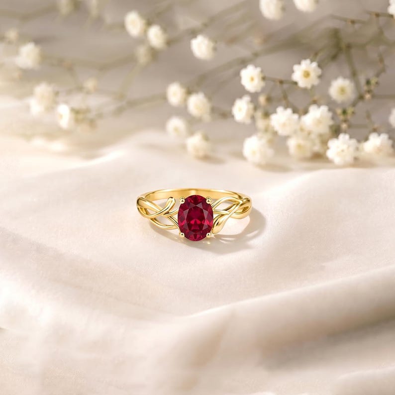 K&ouml;nnte beinhalten: Ein Goldring mit einem zentralen, oval geschliffenen, tiefroten Edelstein, der von vier Krappen gehalten wird. Die Ringschiene ist mit einem filigranen, rankenartigen Design gestaltet, das sich von der Mitte aus verzweigt und flie&szlig;t.