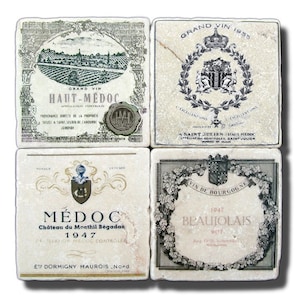 May include: Four square white coasters with black and gold vintage wine label designs. The coasters feature the names "Haut-Medoc", "Saint Julien", "Medoc", and "Beaujolais".