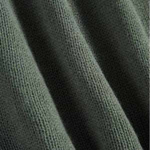 Peut inclure: Gros plan sur un tissu en tricot vert olive textur&eacute;. Le tissu est pli&eacute;, cr&eacute;ant des ombres douces et mettant en valeur le tissage d&eacute;taill&eacute;. La couleur est une tonalit&eacute; sourde et terreuse, sugg&eacute;rant un textile confortable.