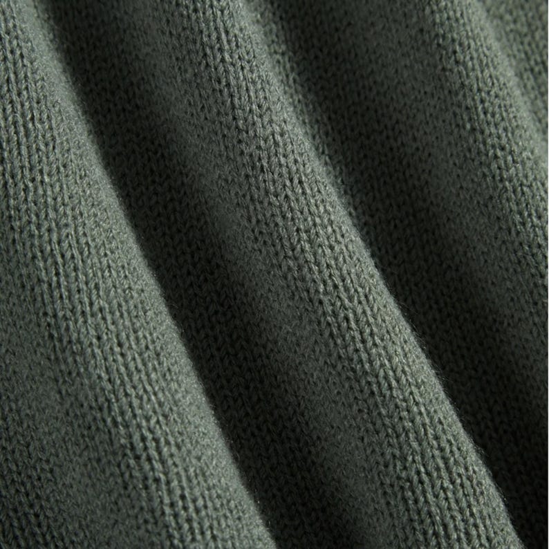 Peut inclure: Gros plan sur un tissu en tricot vert olive textur&eacute;. Le tissu est pli&eacute;, cr&eacute;ant des ombres douces et mettant en valeur le tissage d&eacute;taill&eacute;. La couleur est une tonalit&eacute; sourde et terreuse, sugg&eacute;rant un textile confortable.