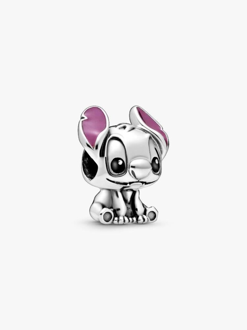 May include: A silver-colored charm featuring the character Stitch from the Disney movie Lilo & Stitch. The charm has large ears with pink accents, black eyes, and a small nose. The charm is sitting down.