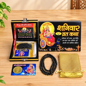 May include: A black box set containing a Siddha Shri Shani Kavach, a black bead mala, a gold-colored coin, and a gold fabric pouch. The box lid features an illustration of a deity in a chariot with a crow and Hindi text including Shaniwar Vrat Katha.