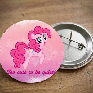 May include: A round, pink button with a cartoon pony illustration and the text "Too cute to be quiet!" The pony is pink with a curly mane and tail. The button has a metal pin back.