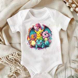 May include: White baby bodysuit featuring a colorful graphic of several cartoon characters. The design includes a red dragon, a yellow Pikachu, a pink creature, a blue turtle-like character, and an orange creature. The graphic is surrounded by colorful paint splatters.