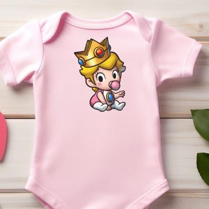 May include: A light pink baby onesie featuring a cartoon illustration of Princess Peach from the Super Mario series. The illustration shows Princess Peach wearing a gold crown and a pink outfit. The onesie is made of soft material.
