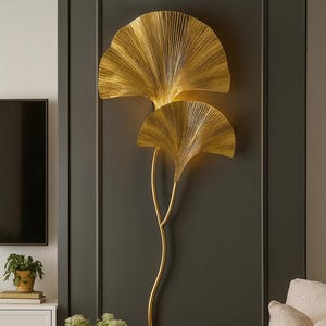 Peut inclure: Applique murale dorée en forme de feuilles de ginkgo, fixée sur un mur gris foncé. La pièce comprend une armoire blanche, une table basse ronde et un canapé beige.