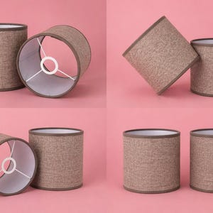 May include: Four cylindrical lampshades in a light brown textured fabric with a darker brown trim. The interior is white, and the shades have a metal frame. The lampshades are designed to fit on a lamp base and diffuse light.