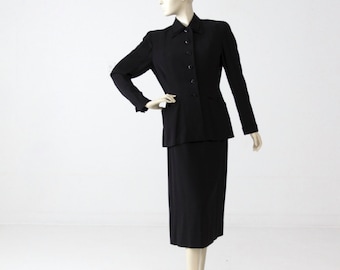 May include: A black skirt suit with a button-up jacket and a straight skirt.
