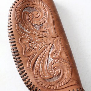 May include: A brown leather clutch with intricate floral tooling and a stitched edge.
