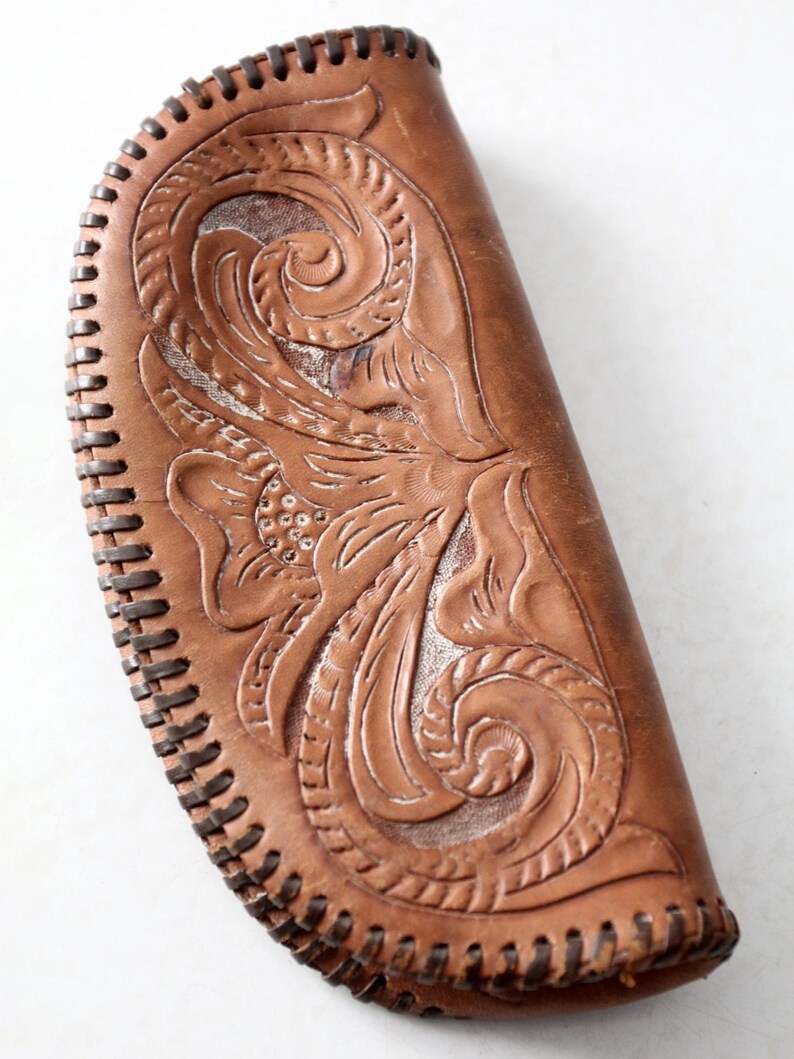 May include: A brown leather clutch with intricate floral tooling and a stitched edge.
