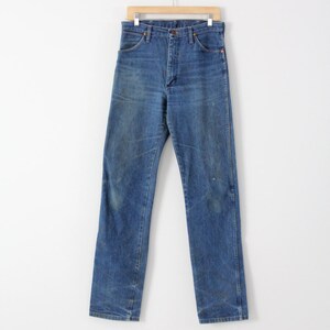 K&ouml;nnte beinhalten: Eine blaue Jeans aus Denim, die an einem Holzb&uuml;gel h&auml;ngt. Die Jeans hat einen klassischen geraden Schnitt und ist aus strapazierf&auml;higem, ausgebleichtem Denim-Stoff gefertigt.
