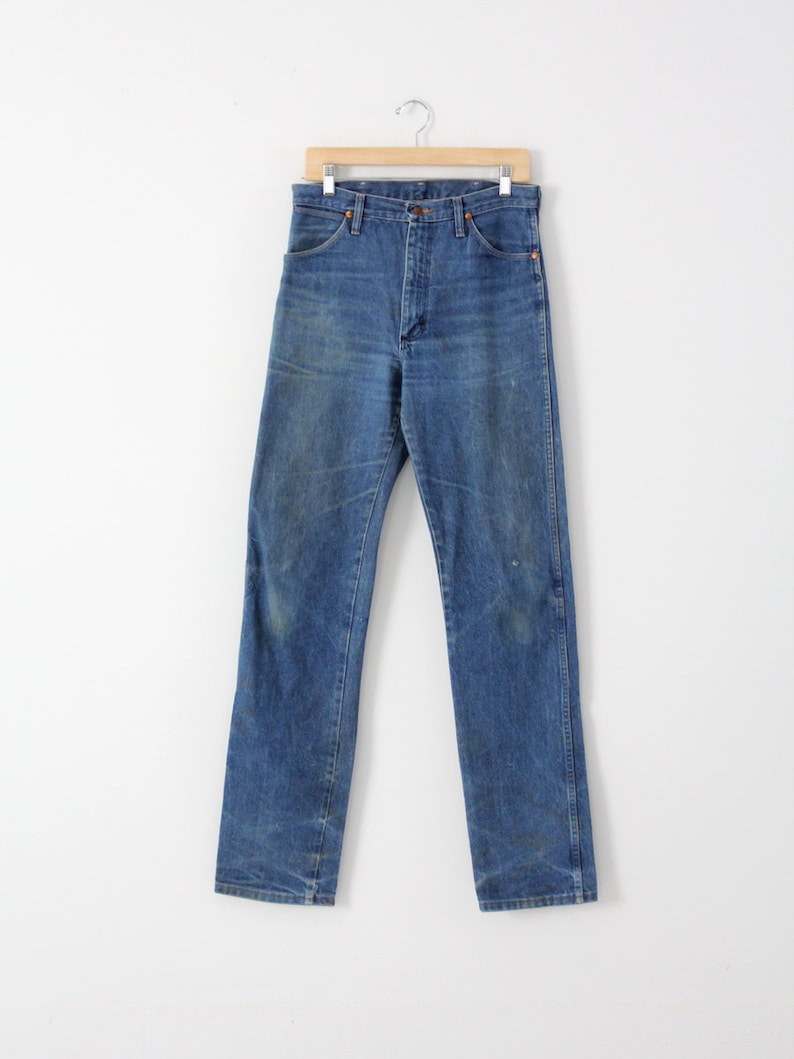 K&ouml;nnte beinhalten: Eine blaue Jeans aus Denim, die an einem Holzb&uuml;gel h&auml;ngt. Die Jeans hat einen klassischen geraden Schnitt und ist aus strapazierf&auml;higem, ausgebleichtem Denim-Stoff gefertigt.