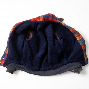 May include: A plaid flannel jacket with a navy blue fleece lining. The jacket is unzipped and turned inside out, showing the fleece lining.