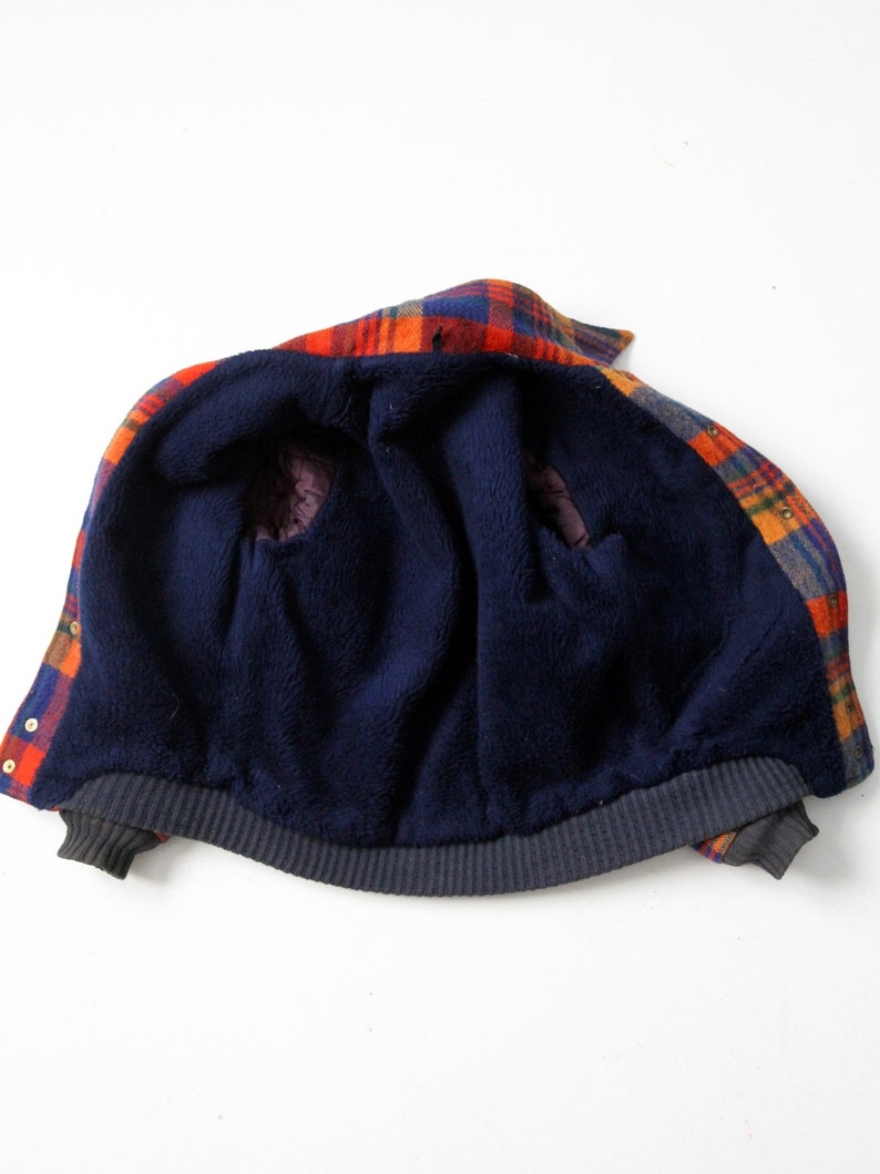 May include: A plaid flannel jacket with a navy blue fleece lining. The jacket is unzipped and turned inside out, showing the fleece lining.