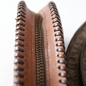 May include: Close-up of a brown leather zipper with a brown stitched edge.