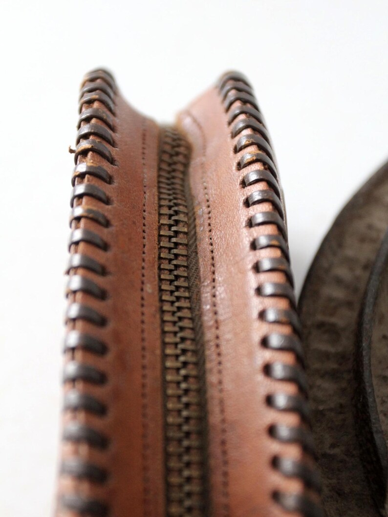 May include: Close-up of a brown leather zipper with a brown stitched edge.