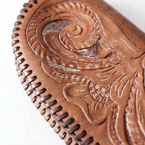 May include: A brown leather wallet with a floral design embossed on the front. The wallet has a stitched edge.