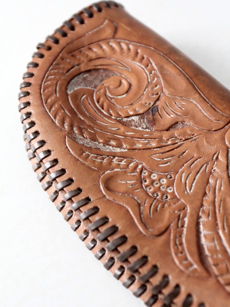 May include: A brown leather wallet with a floral design embossed on the front. The wallet has a stitched edge.