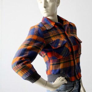 May include: A cropped plaid jacket with orange, blue, and brown colors. The jacket has a button closure and two flap pockets.