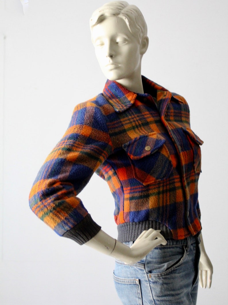 May include: A cropped plaid jacket with orange, blue, and brown colors. The jacket has a button closure and two flap pockets.
