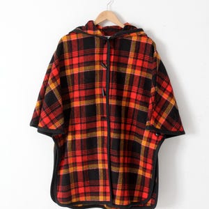 May include: A red, black, and yellow plaid hooded cape with a black trim. The cape has a toggle closure at the neck.