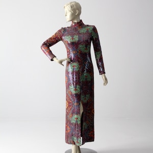 Puede incluir: Un vestido largo de lentejuelas con cuello alto y una abertura en la parte delantera. El vestido es una mezcla de colores púrpura, verde y naranja con un estampado floral.