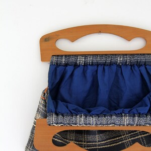 May include: A blue and white plaid fabric bag with wooden handles. The bag has a blue lining and is open to reveal the interior.
