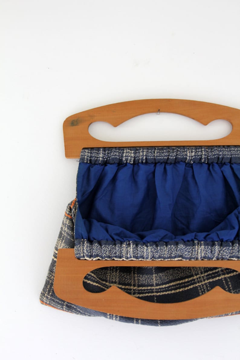 May include: A blue and white plaid fabric bag with wooden handles. The bag has a blue lining and is open to reveal the interior.