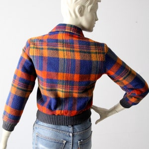 May include: A blue, orange, and brown plaid jacket with a ribbed knit waistband. The jacket is made of a soft, fuzzy material.