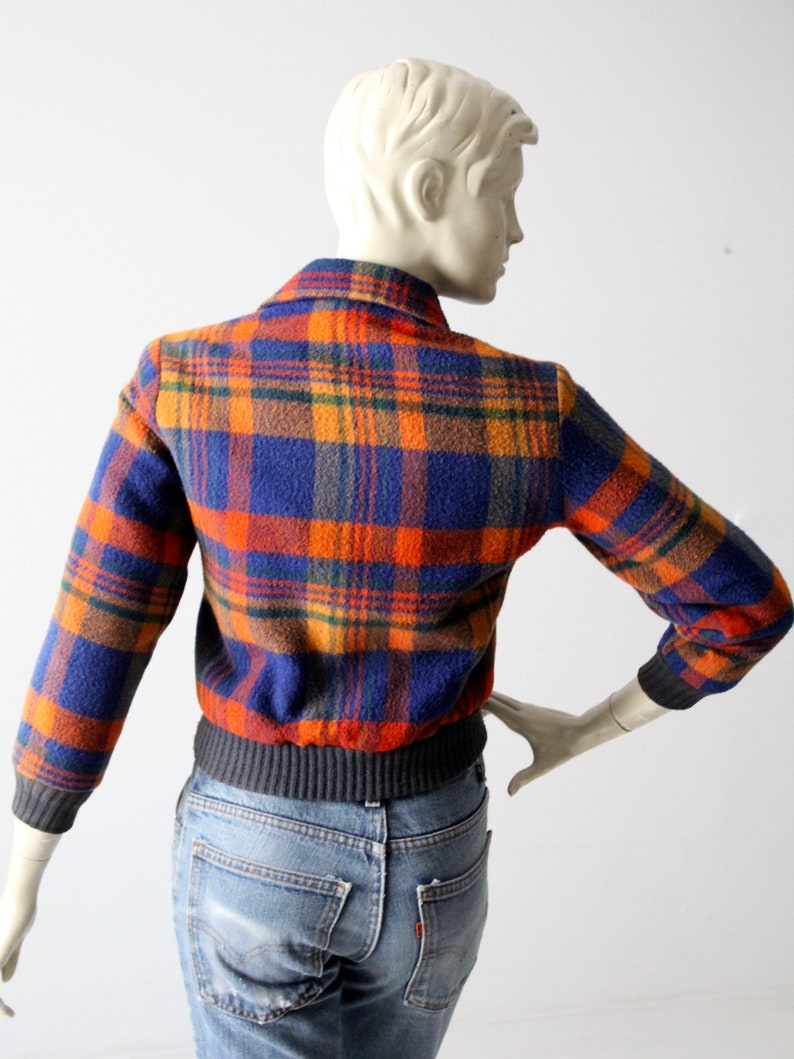 May include: A blue, orange, and brown plaid jacket with a ribbed knit waistband. The jacket is made of a soft, fuzzy material.