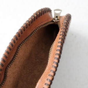 May include: A brown leather pouch with a zipper closure and a decorative stitched edge. The pouch is open and the inside is visible.