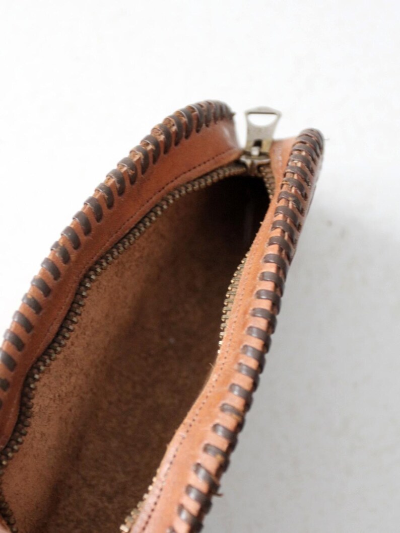 May include: A brown leather pouch with a zipper closure and a decorative stitched edge. The pouch is open and the inside is visible.