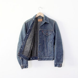 May include: A blue denim jacket with a gray flannel lining. The jacket has a button closure, two front pockets, and a single chest pocket.