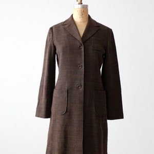 May include: A brown long-sleeved coat with a button-up front and two patch pockets. The coat is made of a textured fabric.