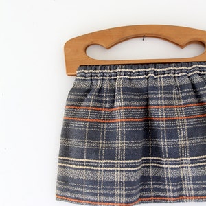 May include: A vintage plaid fabric tote bag with a wooden handle. The bag is blue, white, and orange plaid.