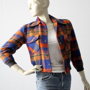 May include: A blue, orange, and brown plaid flannel jacket with a button-up front and two flap pockets. The jacket has a cropped length and a ribbed knit trim at the cuffs and hem.